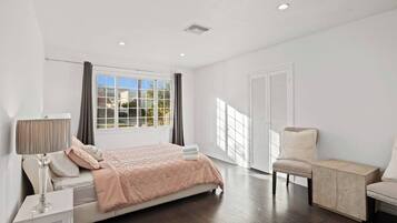 A bedroom with a bed, bedside table, lamp, chair, and a window with curtains.