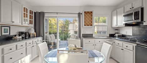 A modern kitchen with white cabinetry, a glass dining table, and a view of the outdoors.