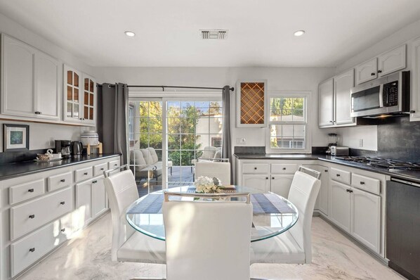 A modern kitchen with white cabinetry, a glass dining table, and a view of the outdoors.