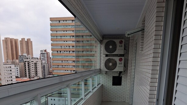 Uma varanda estreita com piso de azulejos, guarda-corpo de vidro e duas unidades de ar condicionado LG fixadas na parede.