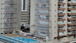 Um edifício alto com várias varandas, piscina e um pátio.
