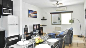 A dining area with a table set for four, a microwave, a refrigerator, a television, and a sofa in the background. - CABO DOWNTOWN STUDIOS: 2BR Studio in heart of town walk anywhere #2 (Cabo San Lucas)
