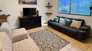 A living room with a sofa, a patterned rug, a TV on a black cabinet, and a window with a view. - CABO DOWNTOWN STUDIOS: 2BR Studio in heart of town walk anywhere #2 (Cabo San Lucas)