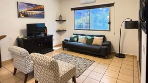 A living room with a sofa, two patterned chairs, a television on a cabinet, a window with a view, and a floor lamp. - CABO DOWNTOWN STUDIOS: 2BR Studio in heart of town walk anywhere #2 (Cabo San Lucas)