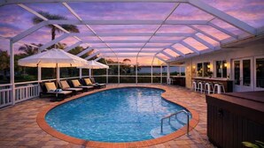 Piscina techada con sillas de descanso y sombrillas, un área de bar y vista al cielo.