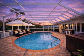 Ein überdachter Pool mit Liegestühlen, Sonnenschirmen, einer Bar und Blick auf den Himmel.