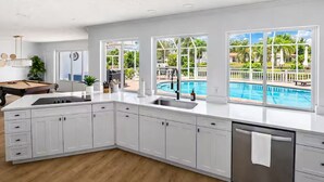 Una cocina moderna con vistas a una piscina, armarios blancos y lavavajillas.