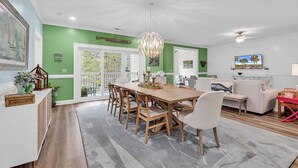 Een eetgedeelte met een houten tafel en stoelen, een kroonluchter, en uitzicht op de omgeving via een glazen deur.