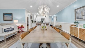 Een ruime eethoek met een lange houten tafel, omringd door stoelen, en een moderne kroonluchter.