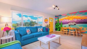Una sala de estar moderna con un sofá azul, una mesa de centro blanca y un mural colorido en la pared.