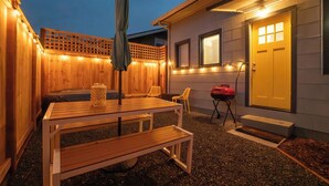 Una terraza de madera con una mesa, sillas, una parrilla y una puerta con ventana.