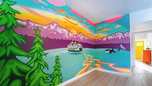 Una habitación con un mural llamativo de un atardecer sobre montañas, un barco y fauna silvestre.