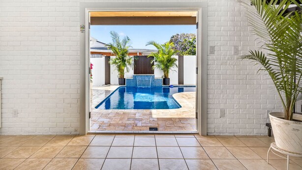 A modern interior with a white brick wall, a tiled floor, and a doorway leading to an outdoor swimming pool area. - Pool Oasis -Near RJ Stadium, Hyde Park & Downtown (Tampa)