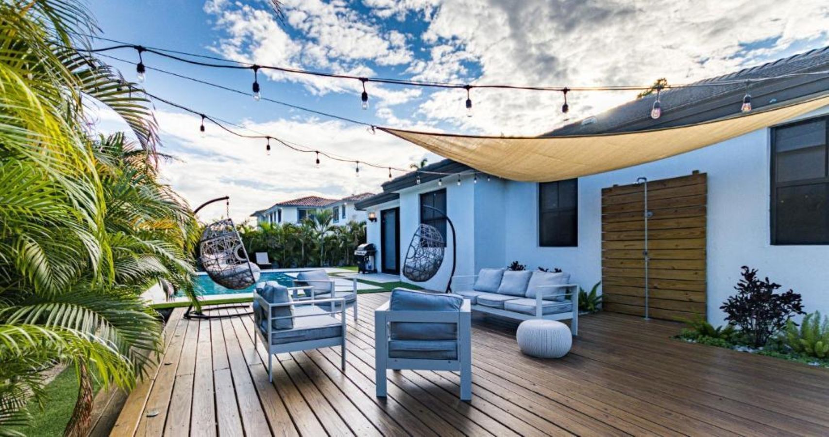 A wooden deck with outdoor furniture, a hanging chair, and a pool.