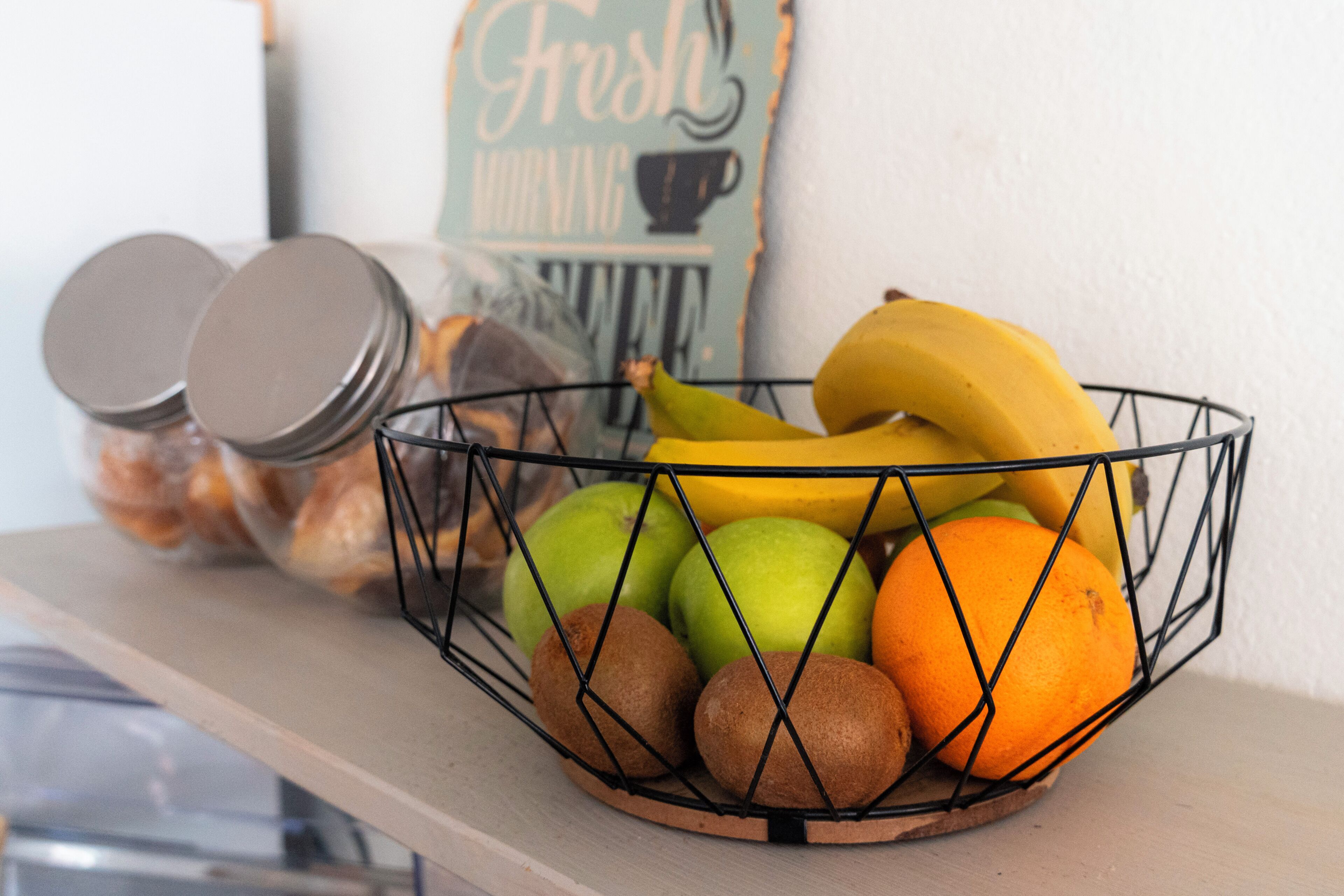 A wire basket containing fruits and a jar with a lid.