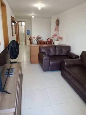 Uma sala de estar com um sofá de couro marrom, uma mesa de centro de madeira e uma área de jantar com mesa e cadeiras.