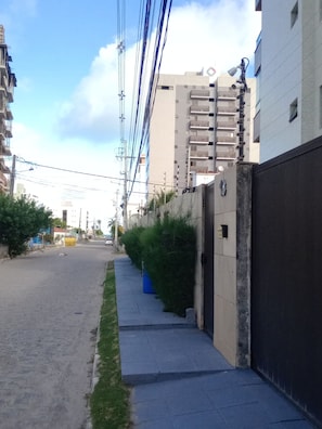 Uma rua estreita urbana com calçada, um edifício com portão e vários postes de eletricidade com fios.
