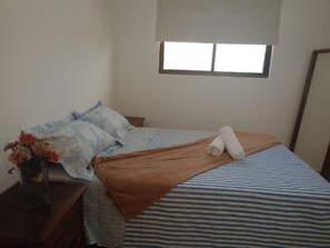 Uma cama bem arrumada com roupa de cama listrada, um cobertor marrom e toalhas enroladas.