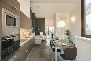 Une cuisine moderne dotée d’appareils électroménagers intégrés, un coin repas avec une table en verre et une vue dégagée sur l’extérieur grâce à une grande fenêtre.