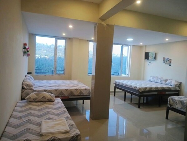 A hotel room with two beds, a large window, and a flat-screen TV on the wall.