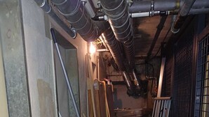 Een kleine, rommelige kamer met een radiator, een metalen hek en verschillende spullen verspreid.
