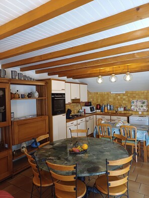 A kitchen with wooden beams, a dining table with chairs, and various kitchen appliances.
