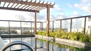Ein Außenpool mit einer Pergola, Glasgeländern und Blick auf die Stadtlandschaft.