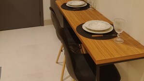Ein kleines Zimmer mit einem Holztisch, gedeckt für zwei Personen, einem schwarzen Stuhl, einem kleinen Regal über dem Tisch und einem weißen, an der Wand befestigten Telefon.