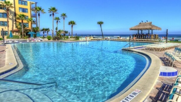 A clear blue pool with a lifeguard stand, lounge chairs, and a thatched umbrella structure.