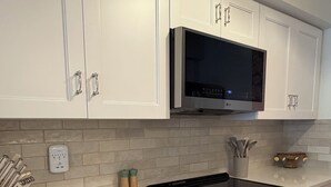 A kitchen with white cabinetry, a black stove, and a microwave above it. - Privateer Beachfront Retreat, Designer Renovation, Ground Floor Beachfront (Fort Myers Beach)