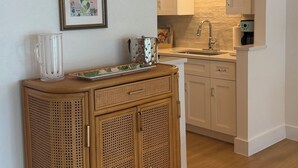 A kitchen with a wooden cabinet, a framed picture, and a sink. - Privateer Beachfront Retreat, Designer Renovation, Ground Floor Beachfront (Fort Myers Beach)