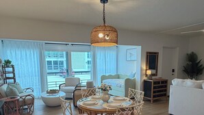 A spacious living room with a dining area, a large window, and a hanging light fixture. - Privateer Beachfront Retreat, Designer Renovation, Ground Floor Beachfront (Fort Myers Beach)