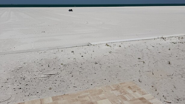 A vast, flat, white sandy area with a clear blue sky and a distant vehicle. - Privateer Beachfront Retreat, Designer Renovation, Ground Floor Beachfront (Fort Myers Beach)