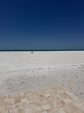 Eine weite, flache, weiße Sandfläche mit blauem Himmel und einem entfernten Fahrzeug.