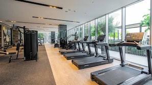 Ein modernes Fitnessstudio mit Laufbändern, Kraftgeräten und einem großen Fenster.