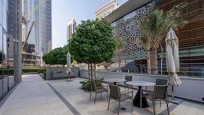 Eine Dachterrasse mit Sitzgelegenheiten im Freien, Palmen und modernen Gebäuden im Hintergrund.
