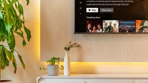 Ein Flachbildfernseher an der Wand zeigt eine Streaming-Oberfläche mit einem Bereich für 'Trending Now'.