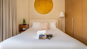 Ein Hotelzimmer mit einem großen Bett, einer runden Wanddekoration, einer Nachttischlampe, einem kleinen Nachttisch mit einer Pflanze sowie einem Schuh- und Handtuchregal auf dem Bett.