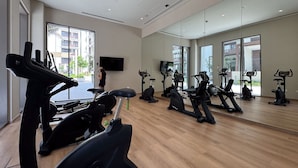 Ein Fitnessstudio mit mehreren Trainingsgeräten, großen Fenstern und einem Flachbildfernseher.