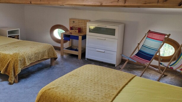 Una habitación con dos camas, un escritorio, una silla y un tragaluz.