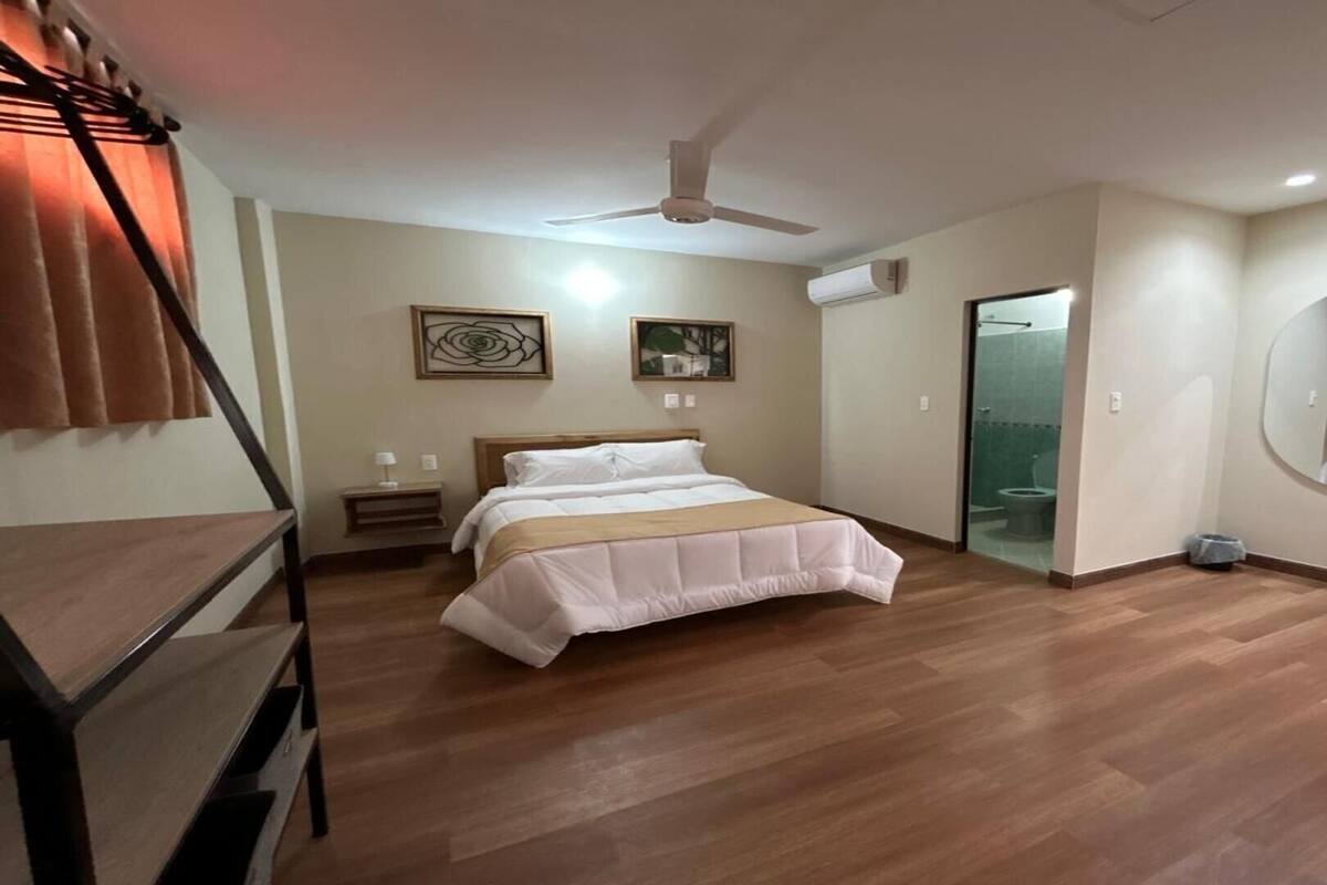 Ett hotellrum med en säng, en takfläkt, en rund spegel och en dörr som leder till ett badrum.