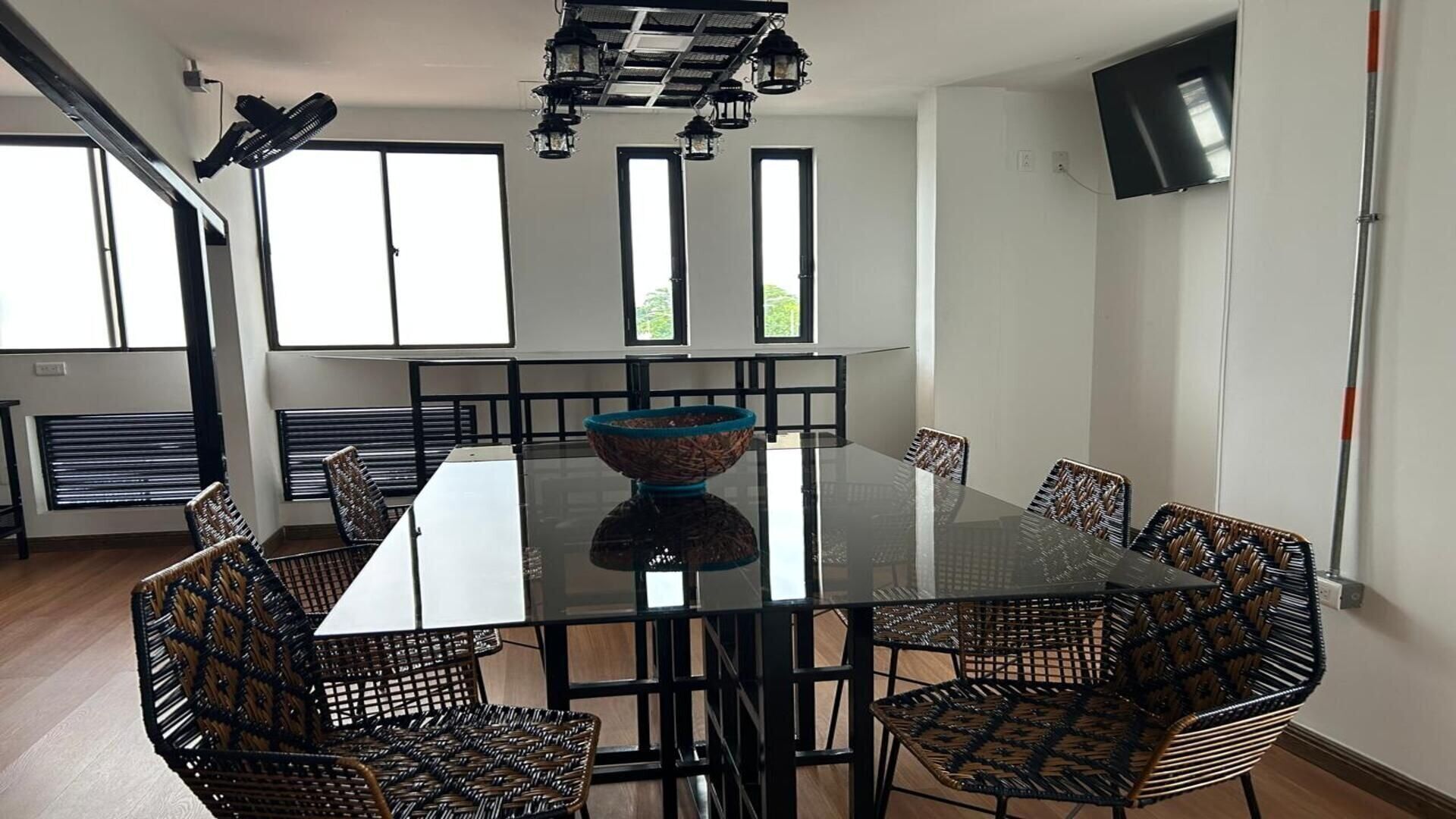 A modern dining room with a glass table, wicker chairs, and a central decorative bowl.