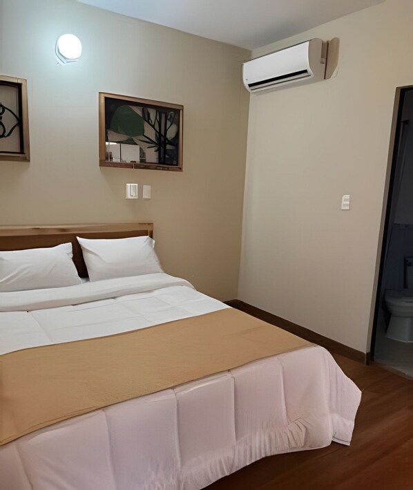 A hotel room with a bed, an air conditioning unit, a painting, and a door leading to a bathroom. - Hotel Coliving Puerto Living (Barrancabermeja)