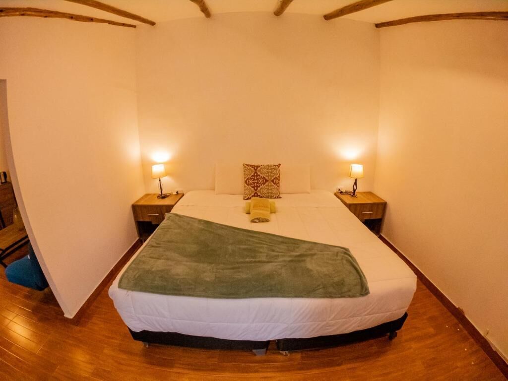 Un dormitorio con una cama, dos mesitas de noche con lámparas, un almohadón y una manta.