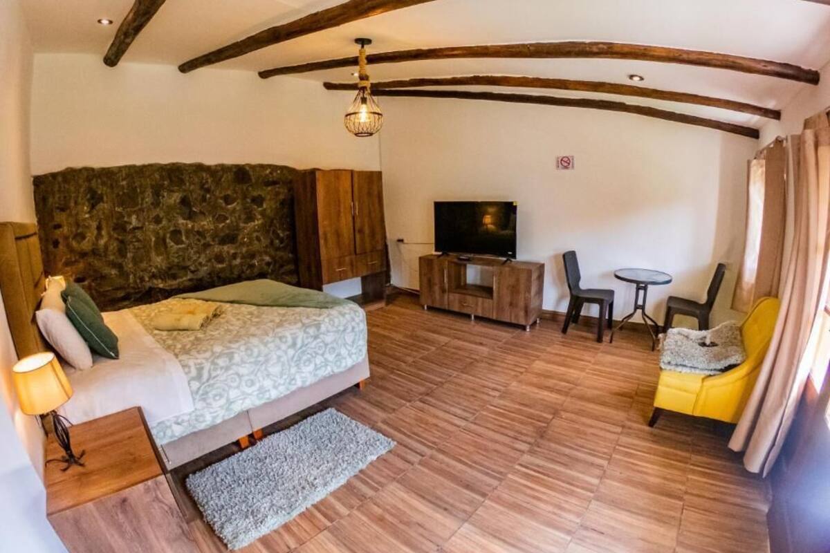 Een slaapkamer met een bed, een televisie, een tafeltje en een gele stoel.