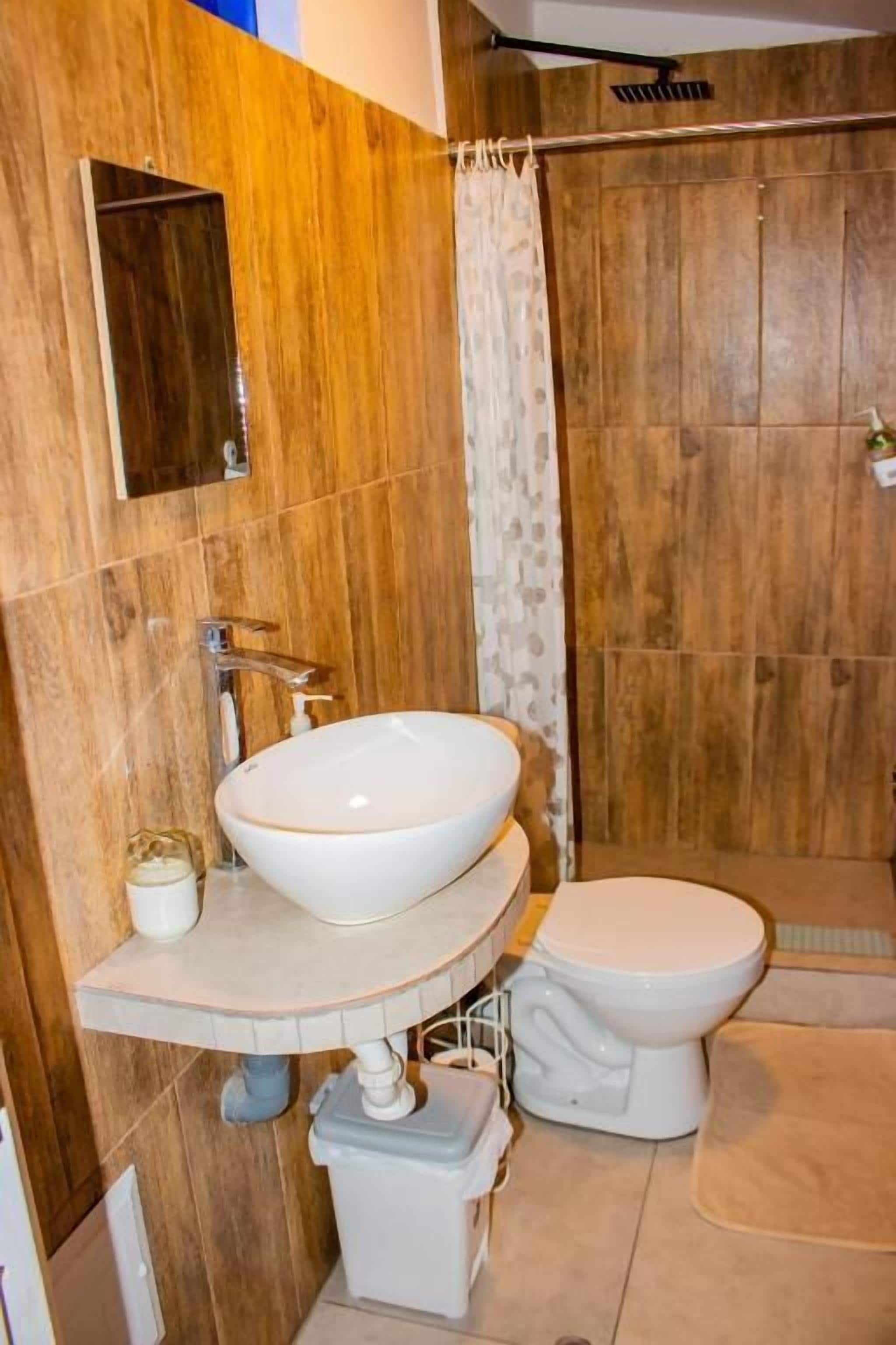 Un baño con pared de madera, un lavamanos blanco, un inodoro y una cortina de ducha.