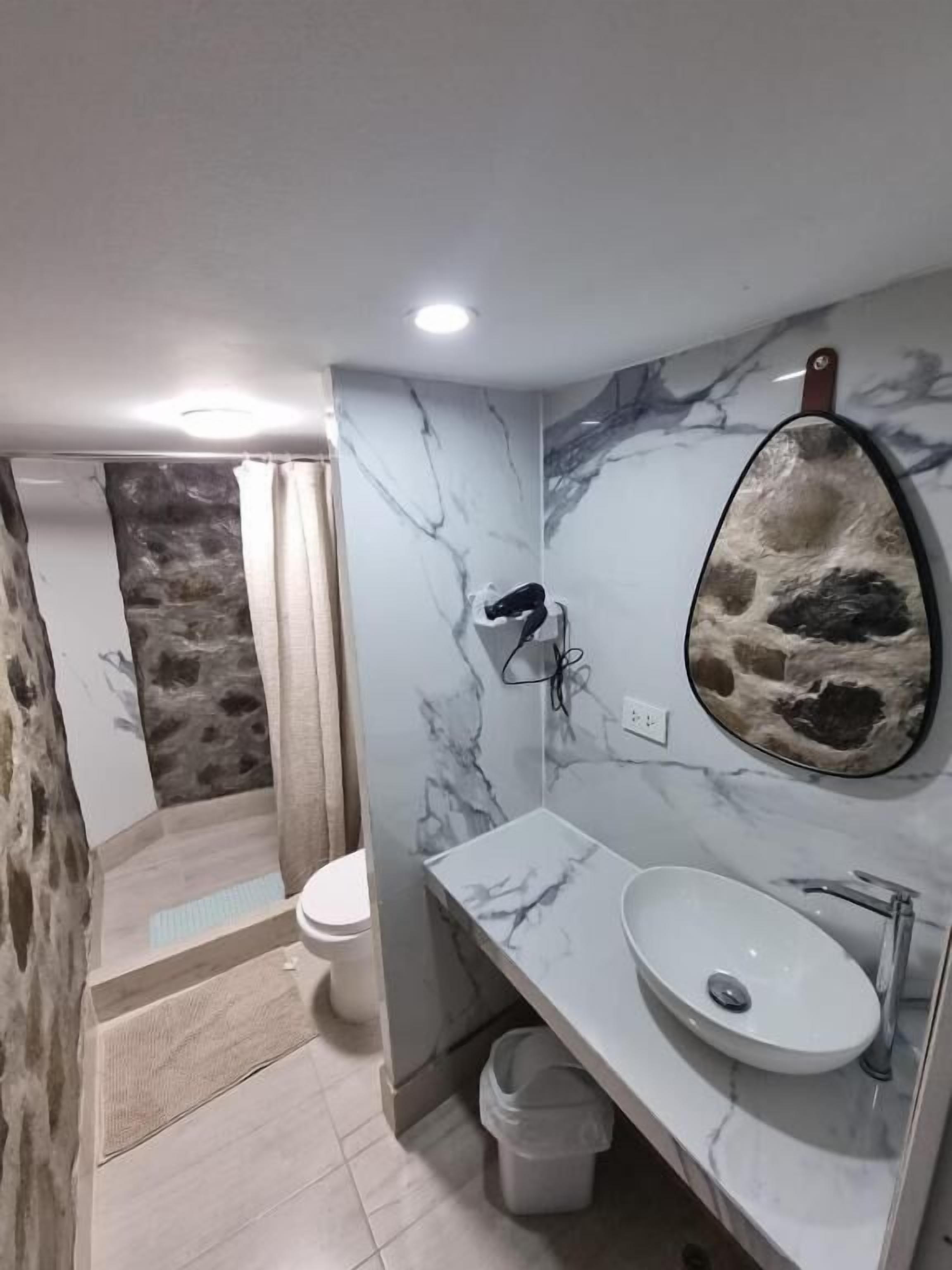 Un baño con lavamanos de mármol, pared de piedra y zona de ducha.