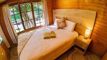 A wooden-paneled room with a large bed, a nightstand, and a window with curtains.