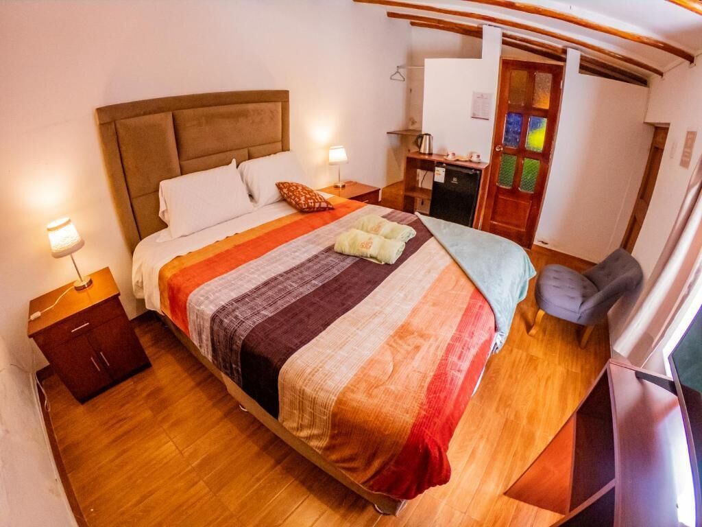 Una cama con una colcha a rayas, una lámpara de noche, un mueble pequeño y un televisor.