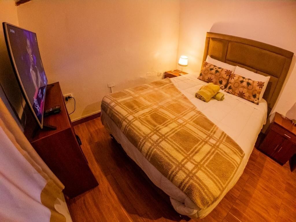 A hotel room with a bed, a television, a nightstand, and a lamp.